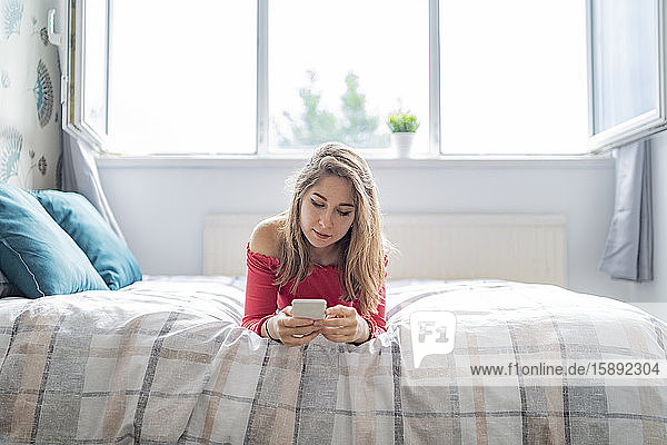 Junge Frau liegt zu Hause im Bett und benutzt ihr Handy