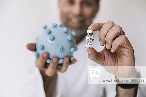 Scientist holding corona virus model and vaccine at desk