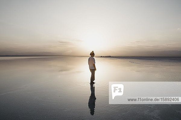 Woman reflecting on water standing at Lake Karum during sunset Danakil Depression Ethiopia Afar