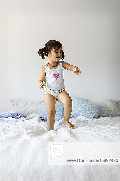 Porträt eines kleinen Mädchens in Unterwäsche beim Tanzen auf dem Bett