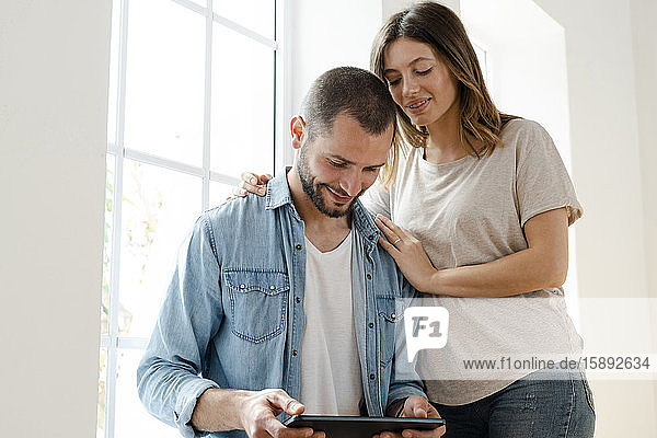 Smiling couple at home in front of window looking at tablet together
