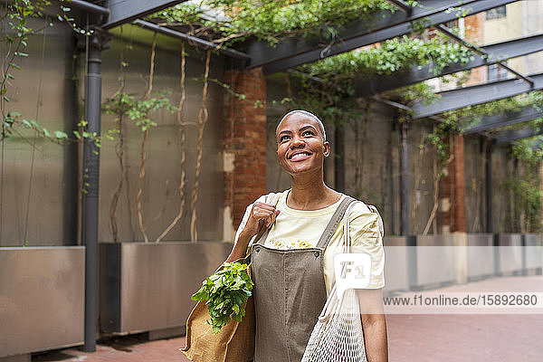 Smiling woman with grocery bag in the city looking up