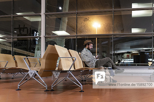 Mann sitzt im Abflugbereich des Flughafens und benutzt ein Smartphone