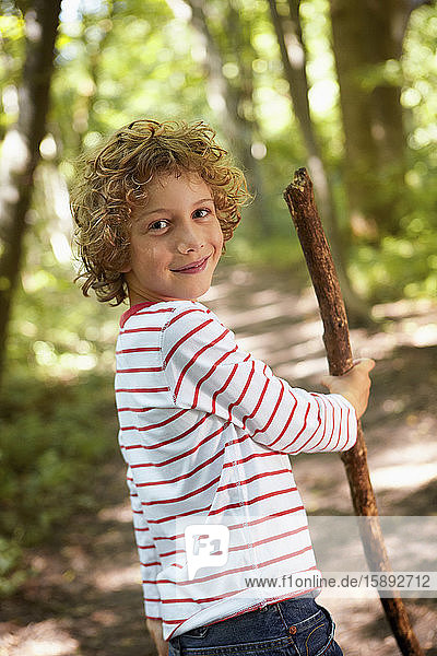 Portrait of boy with wood stick walking in forest