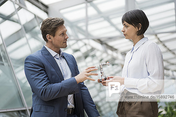 Geschäftsmann und -frau stehen im Atrium eines Bürogebäudes und sprechen über einen Roboterarm