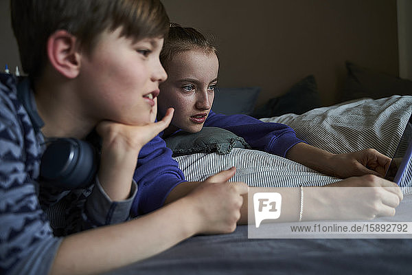 Geschwister  die zusammen auf dem Bett liegen und ein Smartphone für Video-Chat benutzen