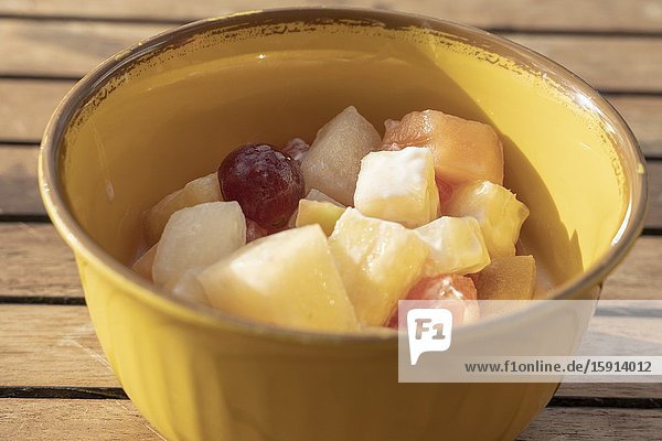 Top view of white bowl full of fruit salad containing strawberries grapes orange kiwi pineapple and apple.