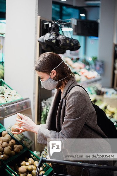 Woman in mask buying fruits at grocery store.