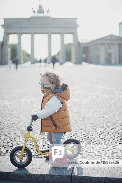 Little boy 2-3 Years old with bicycle and mask in front of Brandenburg gate in Berlin.