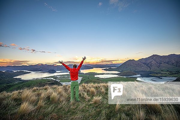 Hiker stretches his arms in the air  panoramic view of Wanaka Lake and mountains at sunset  Rocky Peak  Glendhu Bay  Otago  South Island