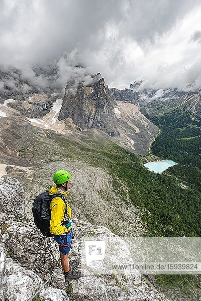 Young man  mountaineer on a fixed rope route  Via Ferrata Vandelli  view of Lago di Sorapis  Sorapiss circuit  mountains with low clouds  Dolomites  Belluno  Italy  Europe