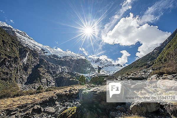 Mountaineer stands on rocks  view of Rob Roy Glacier  Sun Star  Mount Aspiring National Park  Otago  South Island  New Zealand  Oceania