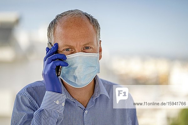 Mann mit Schutzmaske und blauen Latexhandschuhen bei der Benutzung eines Mobiltelefons  Deutschland  Europa