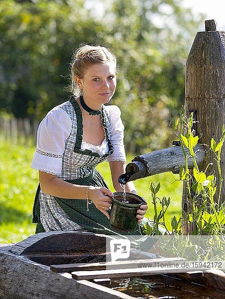 Young woman in dirndl fills a water jug at the well  19 years  Upper Austria  Austria  Europe