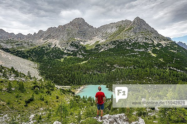 Young man  hiker stands on rocks and looks at turquoise green Sorapiss lake and mountain landscape  Dolomites  Belluno  Italy  Europe