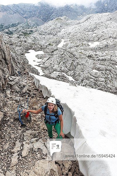 Bergsteigerin auf gesicherter Route neben Schneefeld von Simonyhütte zur Adamekhütte  felsiges alpines Gelände  Salzkammergut  Oberösterreich  Österreich  Europa