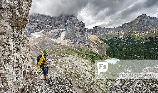Junger Mann  Wanderer an einem Klettersteig  Via Ferrata Vandelli  Blick auf Lago di Sorapis  Sorapiss Umrundung  Berge mit tiefhängenden Wolken  Dolomiten  Belluno  Italien  Europa