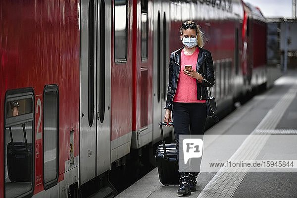 Woman with face mask  waiting for train  on mobile phone  corona crisis  main station  Stuttgart  Baden-Württemberg  Germany  Europe