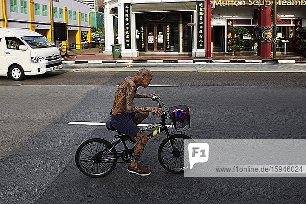 Old Chinese man with tattoos rides a bike in Singapore