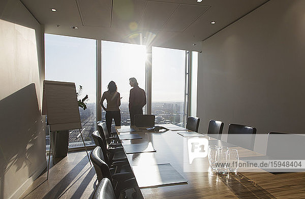 Business people talking at sunny highrise conference room window