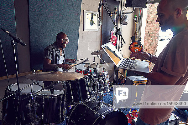 Happy male musicians with drums and laptop in recording studio