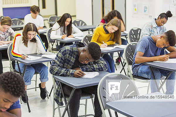 Fokussierte Gymnasiasten  die an Schreibtischen im Klassenzimmer Prüfungen ablegen