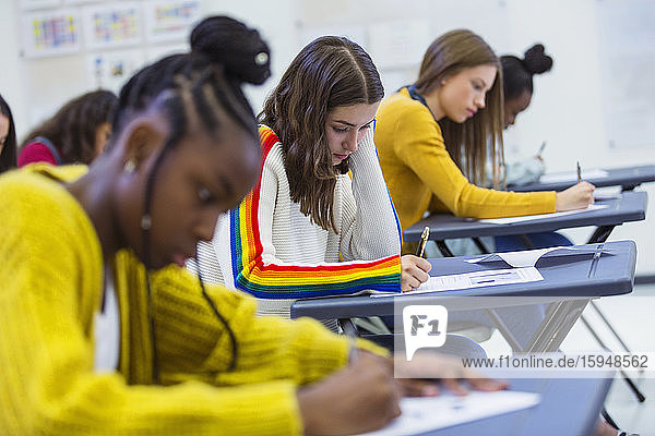 Fokussierte High-School-Schülerinnen  die ihre Prüfung am Schreibtisch im Klassenzimmer ablegen