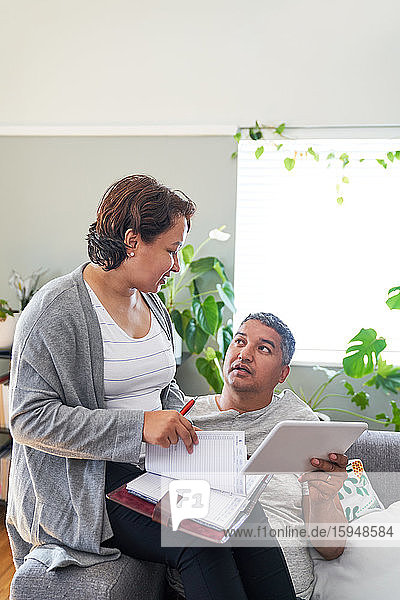 Mature couple with calendar and digital tablet talking in living room