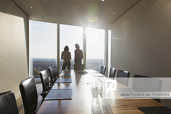 Business people talking at sunny highrise conference room window