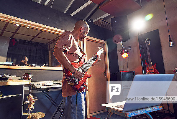 Männlicher Musiker übt Gitarre am Laptop im Aufnahmestudio