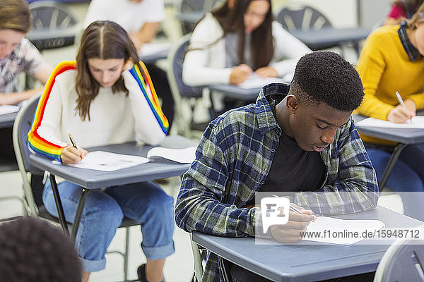 Focused high school boy student taking exam at desk in classroom