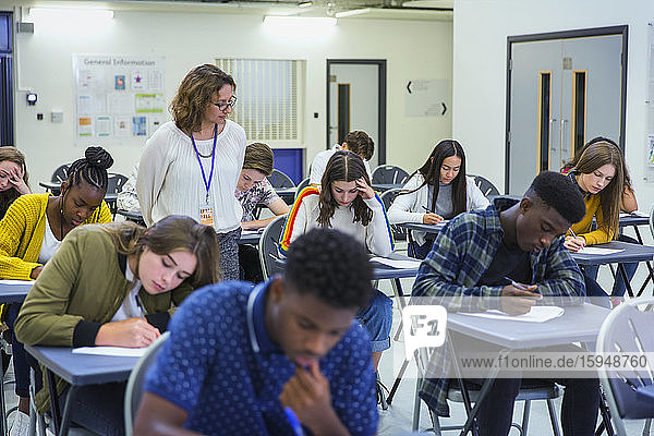 High school teacher supervising students taking exam at desks