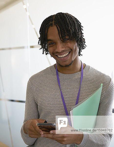 Porträt eines glücklichen Geschäftsmannes  der im Büro mit einem Smartphone simst