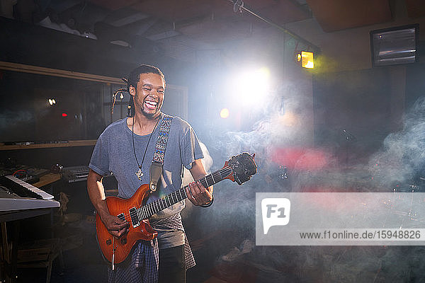 Lächelnder männlicher Musiker spielt E-Gitarre im Aufnahmestudio