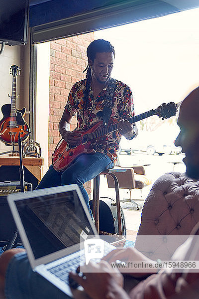 Male musicians with laptop and guitar practicing in recording studio