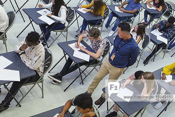 Lehrer beaufsichtigt Gymnasiasten  die am Schreibtisch Prüfungen ablegen
