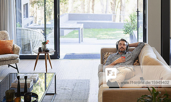 Mann entspannt sich auf dem Wohnzimmersofa  hört Musik mit Kopfhörern und mp3-Player