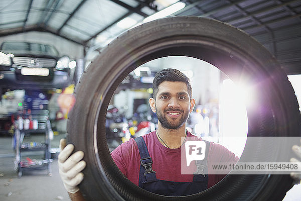 Porträt eines selbstbewussten  lächelnden männlichen Mechanikers  der einen Reifen in einer Autowerkstatt hält