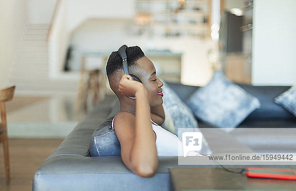 Smiling  serene young woman listening to music with headphones and mp3 player on living room sofa