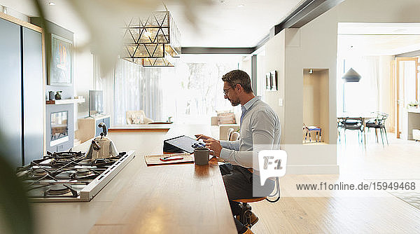 Geschäftsmann am digitalen Tablet  der von zu Hause aus in einer modernen Küche arbeitet