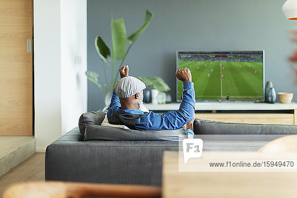 Excited man cheering  watching soccer match on TV in living room