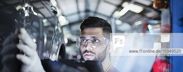 Fokussierter männlicher Mechaniker untersucht Auto in Autowerkstatt