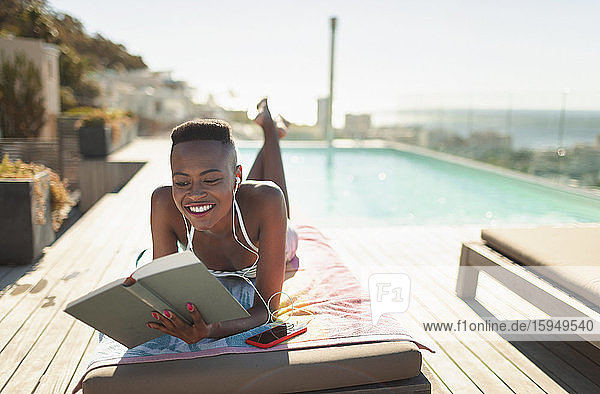 Lächelnde  unbekümmerte junge Frau liest Buch am sonnigen Pool