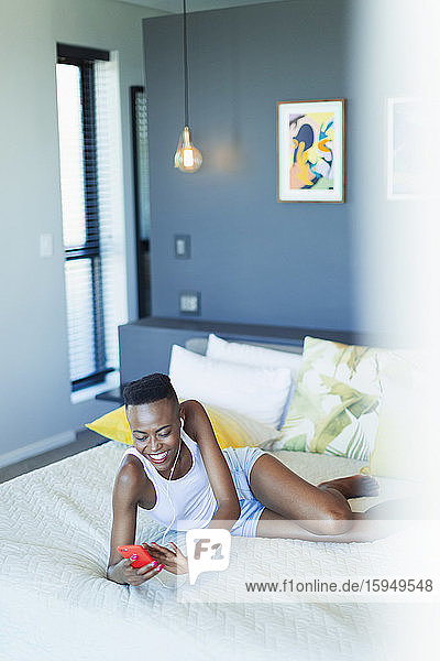 Smiling young woman relaxing on bed  listening to music with headphones and mp3 player