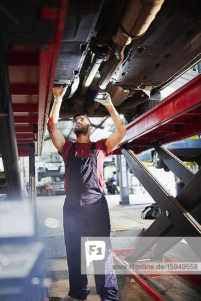 Männlicher Mechaniker  der unter dem Auto in einer Autowerkstatt arbeitet