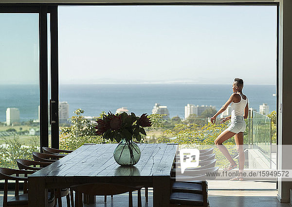 Young woman standing on modern balcony with sunny ocean view