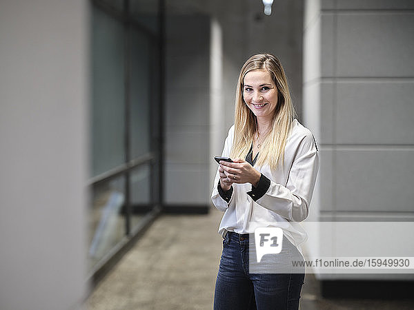 Lächelnde Geschäftsfrau benutzt Handy im modernen Büro