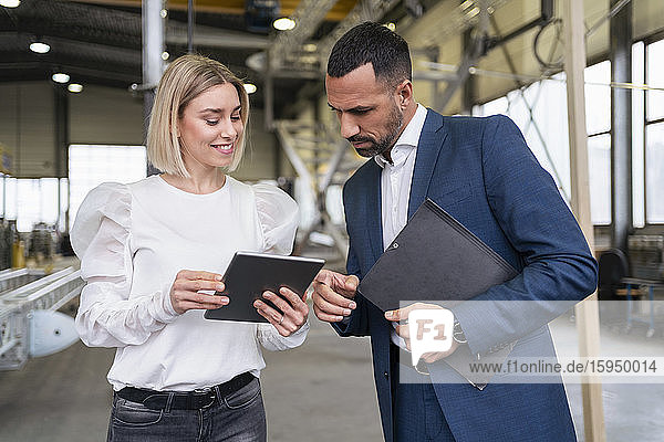 Geschäftsmann und junge Frau mit Tablette im Gespräch in einer Fabrik