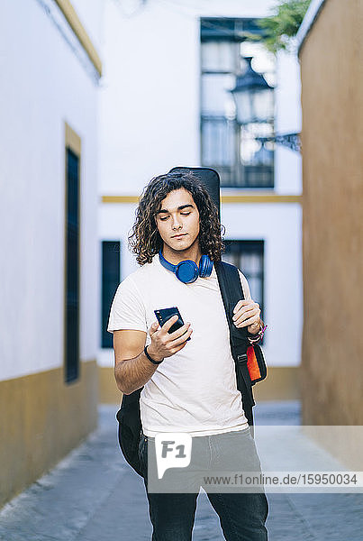 Junger Mann benutzt Mobiltelefon  während er in einer engen Straße in Santa Cruz  Sevilla  Spanien  steht