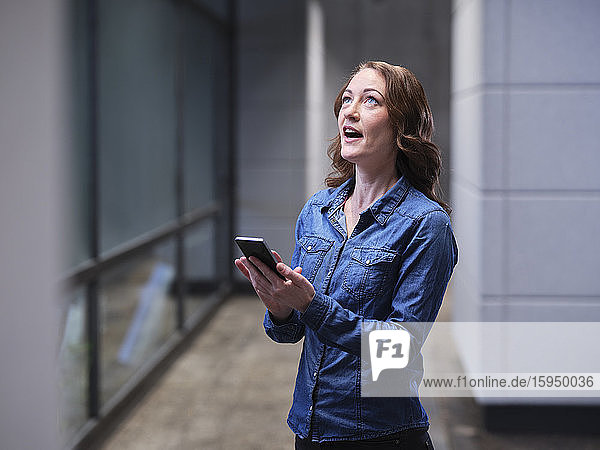 Geschäftsfrau mit Handy in moderner Büroetage mit Blick nach oben